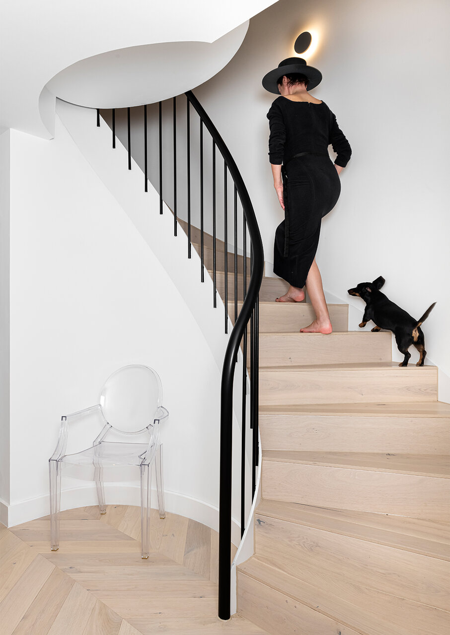 female in long japanese style dress walking with a dog on luxury interior staircase bespoke made with black metal spindles and light oak cladding curated by misch_MISCH studio battersea london